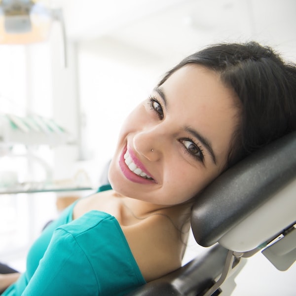 Young woman with dark hair in a green top looking back while reclining in a dental chair